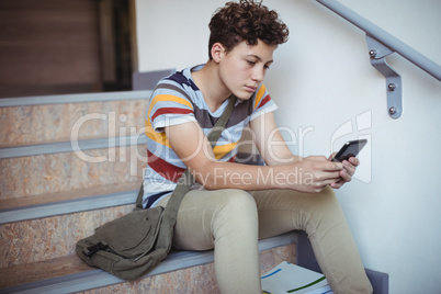 Attentive schoolboy sitting on staircase and using mobile phone