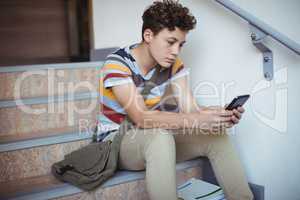 Attentive schoolboy sitting on staircase and using mobile phone