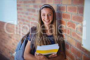 Happy schoolgirl holding books and standing near brick wall