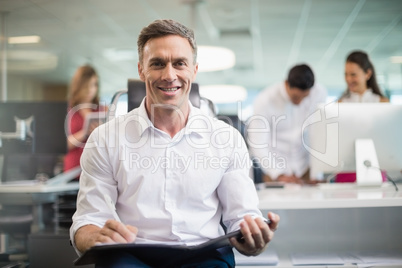 Smiling business executive sitting on chair and writing on clipboard in office