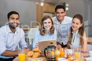 Business colleagues discussing over digital tablet while having breakfast in office cafeteria