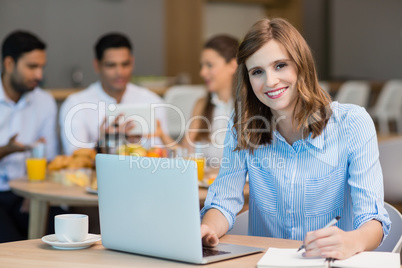 Smiling businesswoman working on laptop while having coffee in office cafeteria
