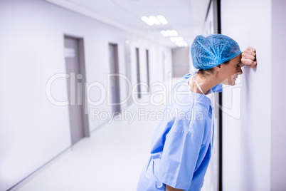 Sad surgeon leaning on wall in corridor