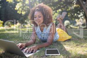 Smiling woman lying on grass and using laptop