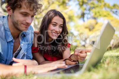 Couple lying on grass and using laptop