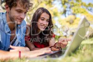Couple lying on grass and using laptop