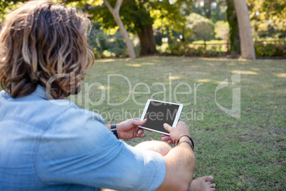 Man sitting on grass using digital tablet