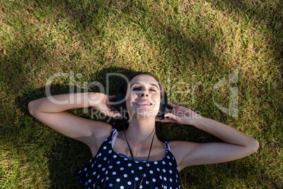 Woman lying on grass and listening to music with headphones