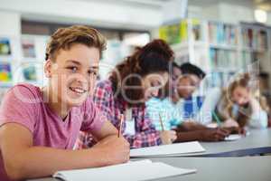 Portrait of happy schoolboy studying in library