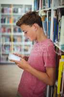 Happy schoolboy using digital tablet in library