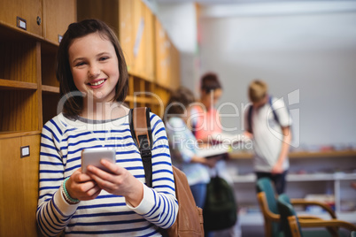 Portrait of happy schoolgirl holding mobile phone in locker room