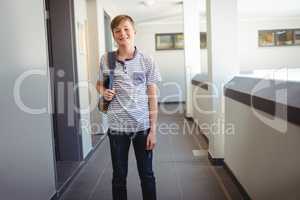 Smiling schoolboy standing with schoolbag in corridor at school