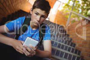 Portrait of schoolboy using mobile phone on staircase