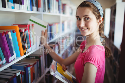 Schoolgirl selecting book from book shelf in library at school