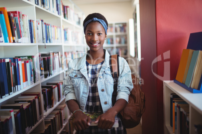 Portrait of schoolgirl standing with books in library