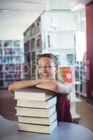 Portrait of happy schoolgirl leaning of stacked books in library