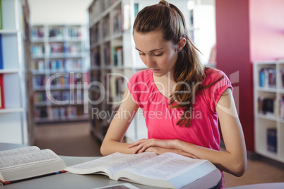 Attentive schoolgirl reading book in library