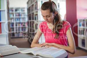 Attentive schoolgirl reading book in library