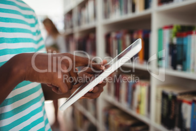 Mid section of schoolboy using digital tablet in library