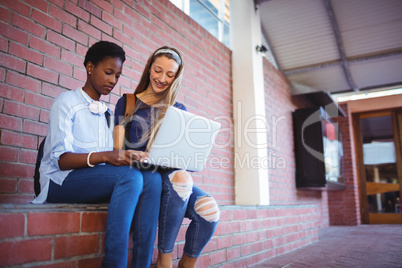Schoolgirls sitting against brick wall and using laptop