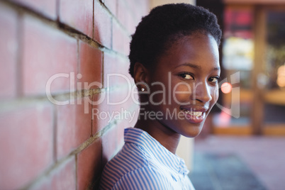 Portrait of happy schoolgirl sitting against brick wall