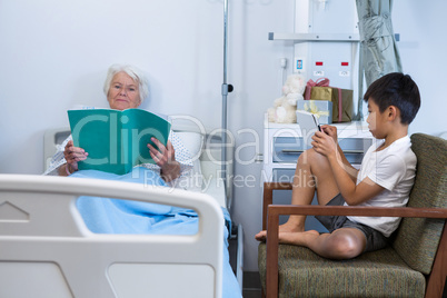 Senior patient reading a book while boy using digital tablet