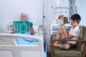 Senior patient reading a book while boy using digital tablet
