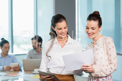 Two female business executives discussing over document in conference room