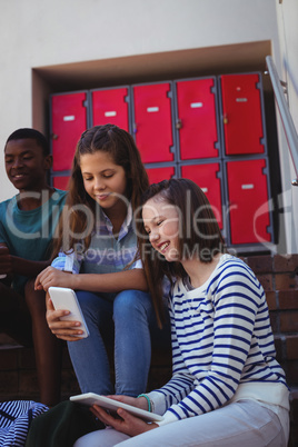 Students using mobile phone and digital tablet on staircase