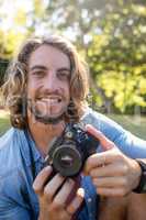 Portrait of man sitting in park with digital camera