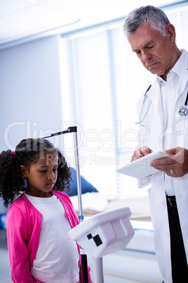 Doctor using digital tablet while measuring height of girl