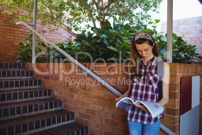 Attentive schoolgirl reading book near staircase