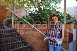 Attentive schoolgirl reading book near staircase