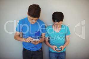 Two kids using mobile phone in corridor at school