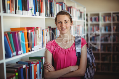Portrait of schoolgirl standing with arms crossed in library