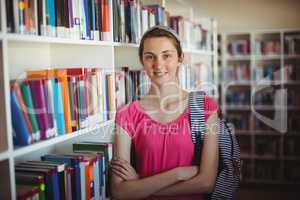 Portrait of schoolgirl standing with arms crossed in library