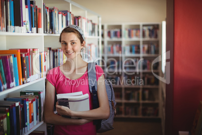 Portrait of schoolgirl standing with books in library