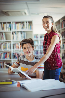 Portrait of happy classmates reading book in library