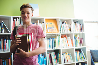 Portrait of happy schoolboy holding book in library