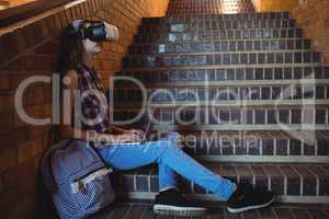 Schoolgirl using virtual reality headset and laptop on staircase