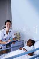 Female doctor writing on clipboard while patient lying on bed at hospital