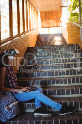 Schoolgirl using virtual reality headset and laptop on staircase