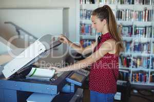 Attentive schoolgirl using Xerox photocopier in library