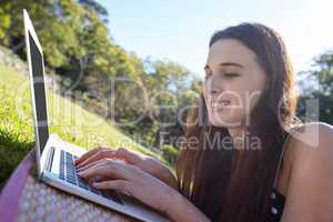 Smiling woman lying on mat and using laptop