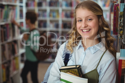 Portrait of happy schoolgirl holding books in library