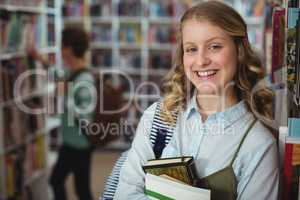 Portrait of happy schoolgirl holding books in library
