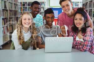 Portrait of happy classmates using laptop in library