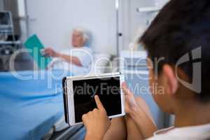 Boy using digital tablet while senior patient reading a book in the background