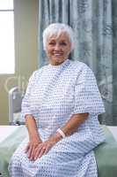 Smiling senior patient sitting on bed in hospital