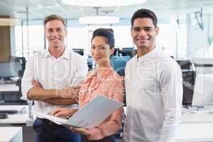 Portrait of smiling business colleagues standing with clipboard at desk